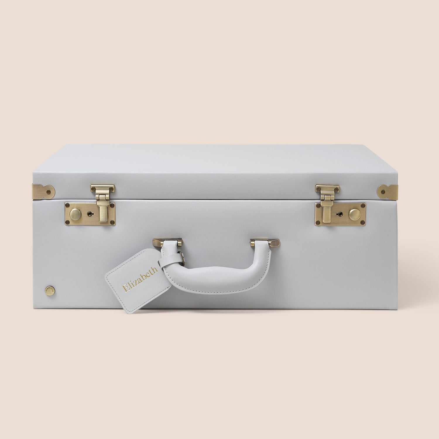 Light gray suitcase with gold hardware on a beige background